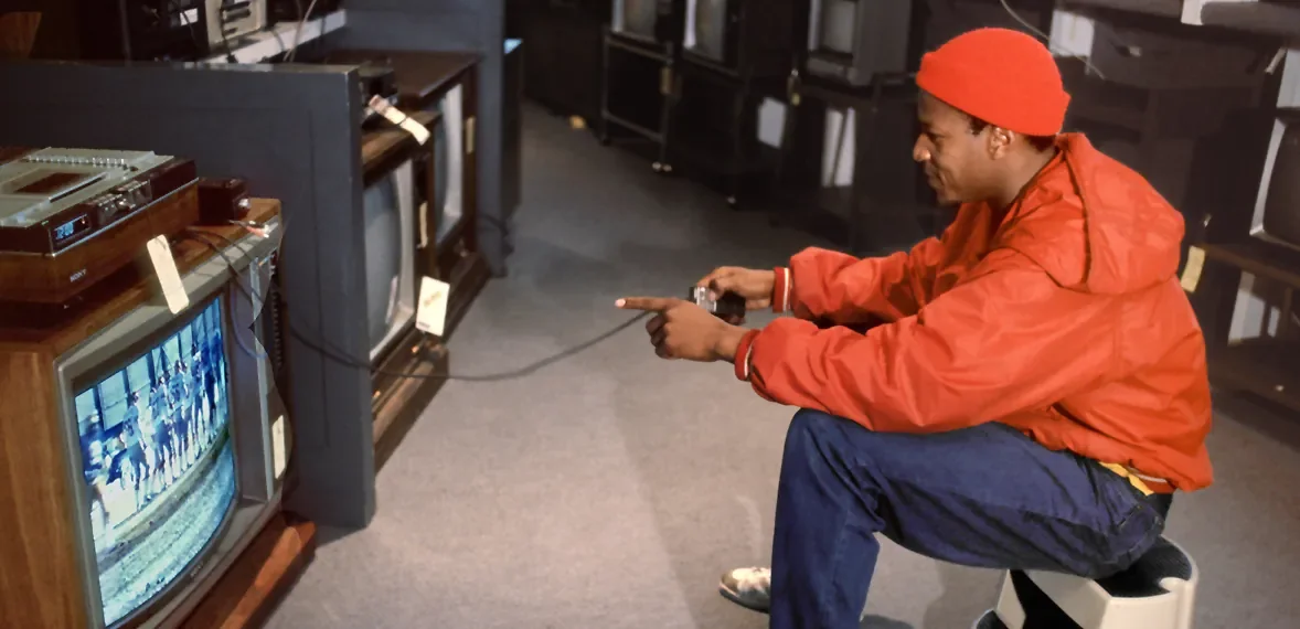 Customer in a red jacket photographing a bank of CRT televisions in an electronics showroom
